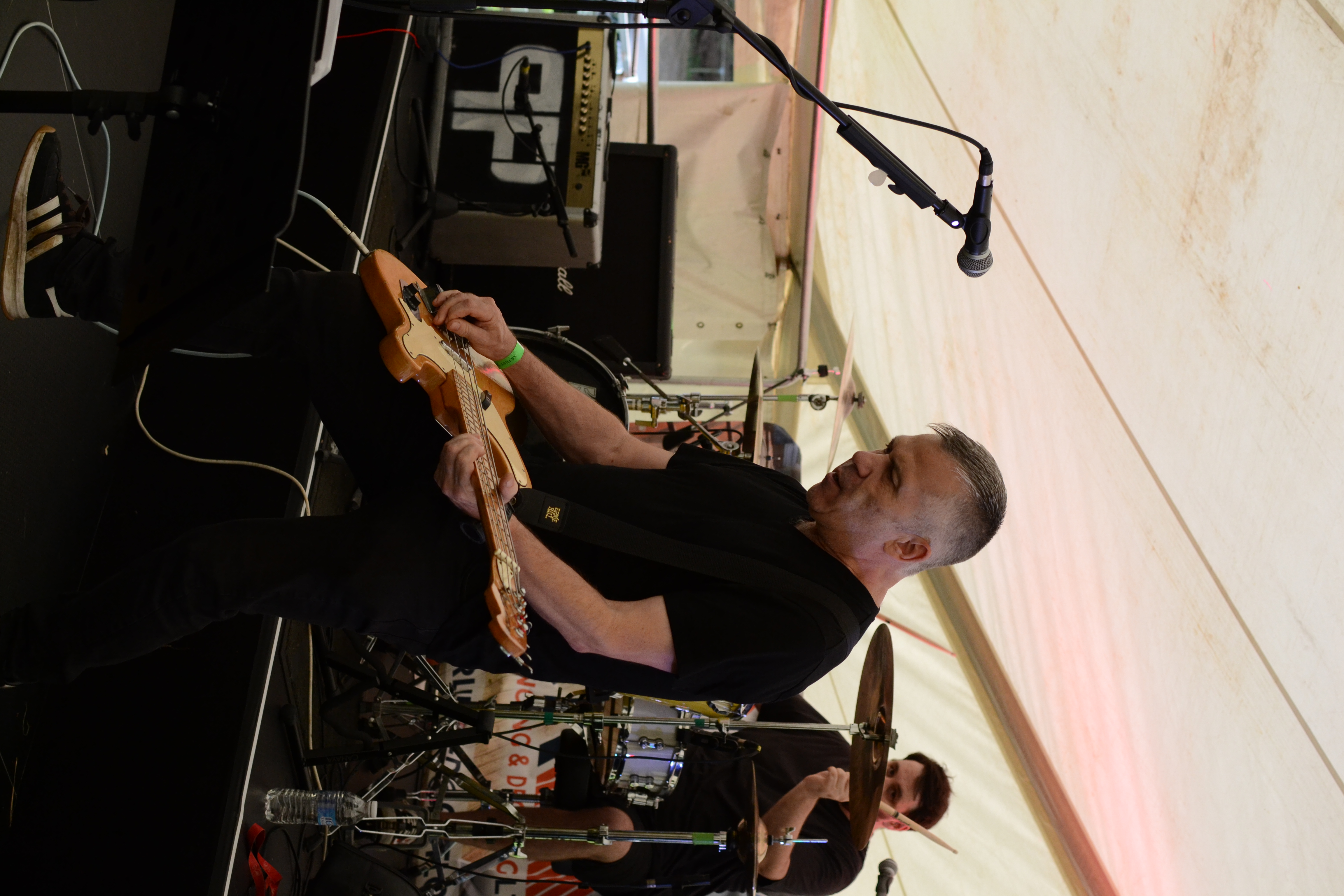 Bassist playing at front of stage with drummer behind under a festival tent