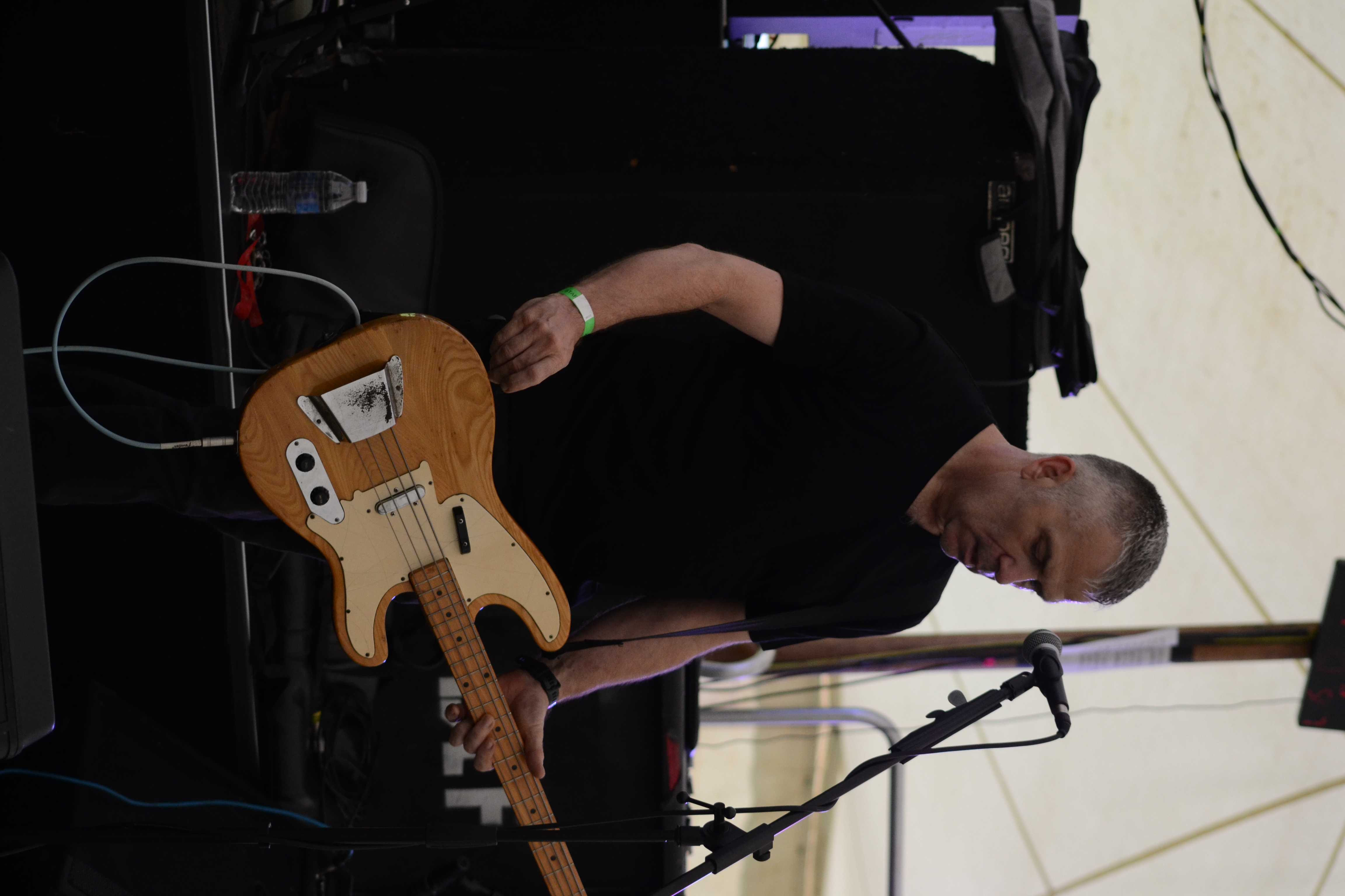Bassist-vocalist standing at the mic with natural wood bass during a live set