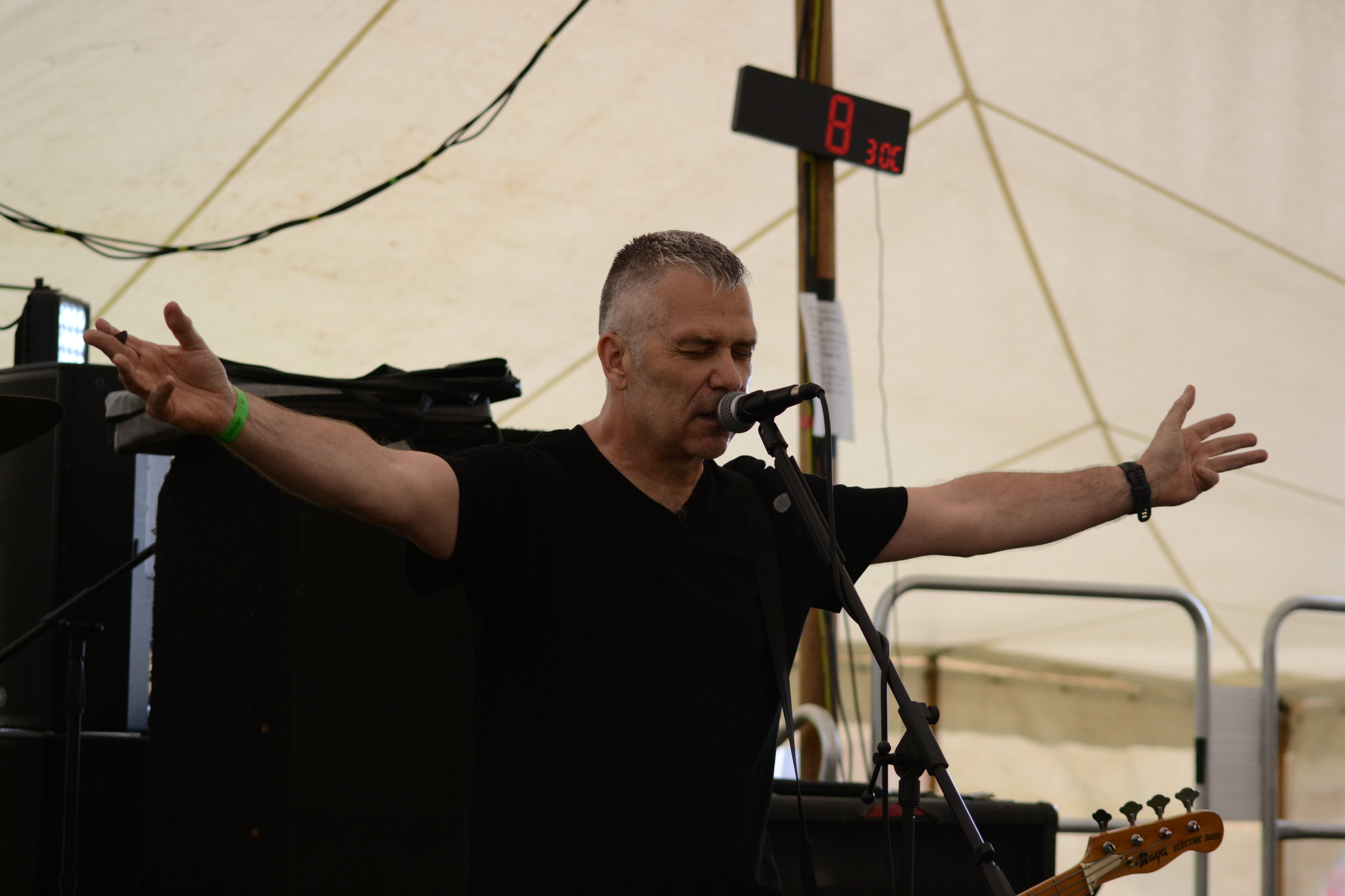 Bassist-vocalist singing with both arms outstretched under the canopy stage