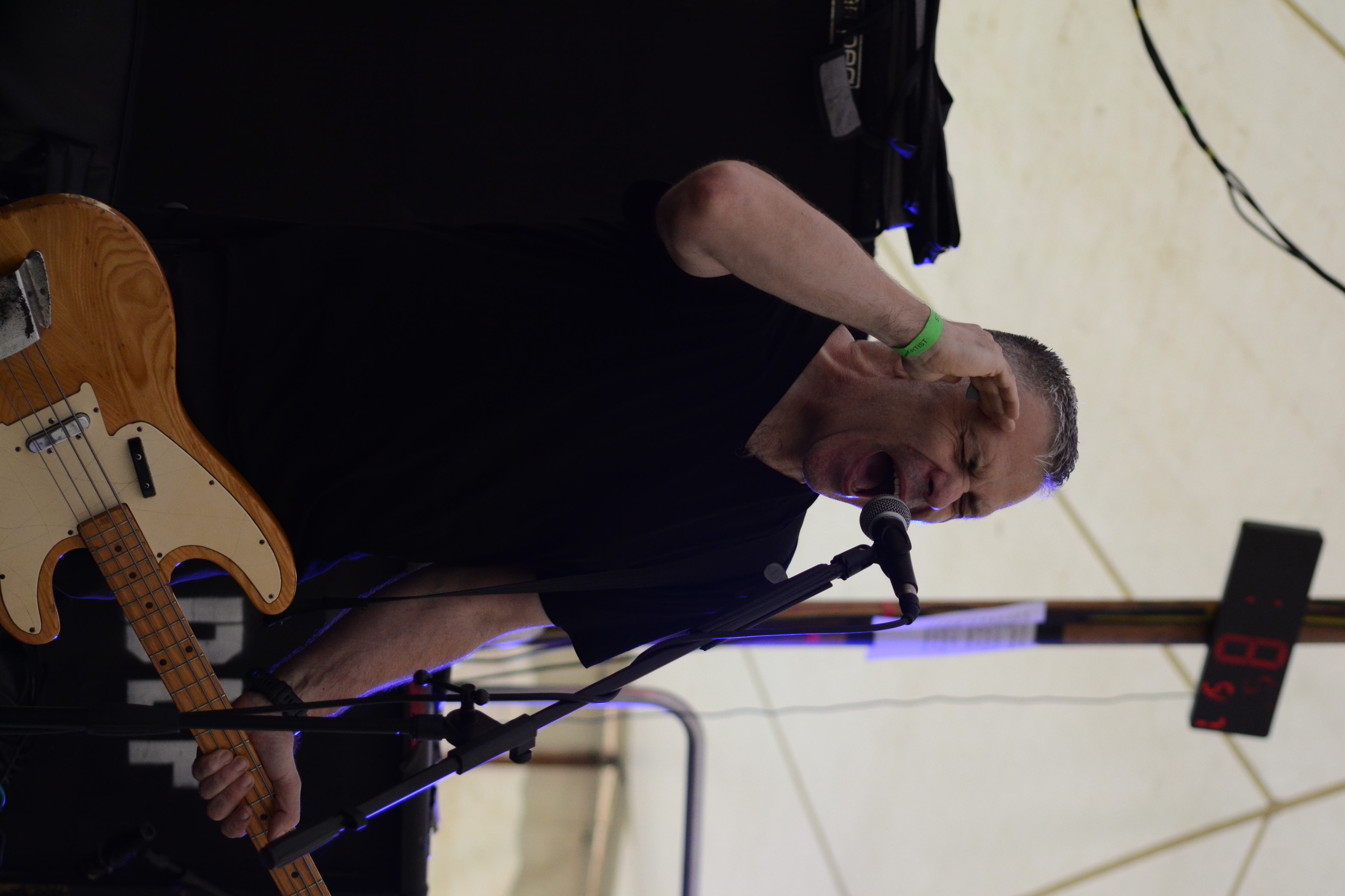 Bassist leaning into the instrument beside stage monitors and speaker stacks