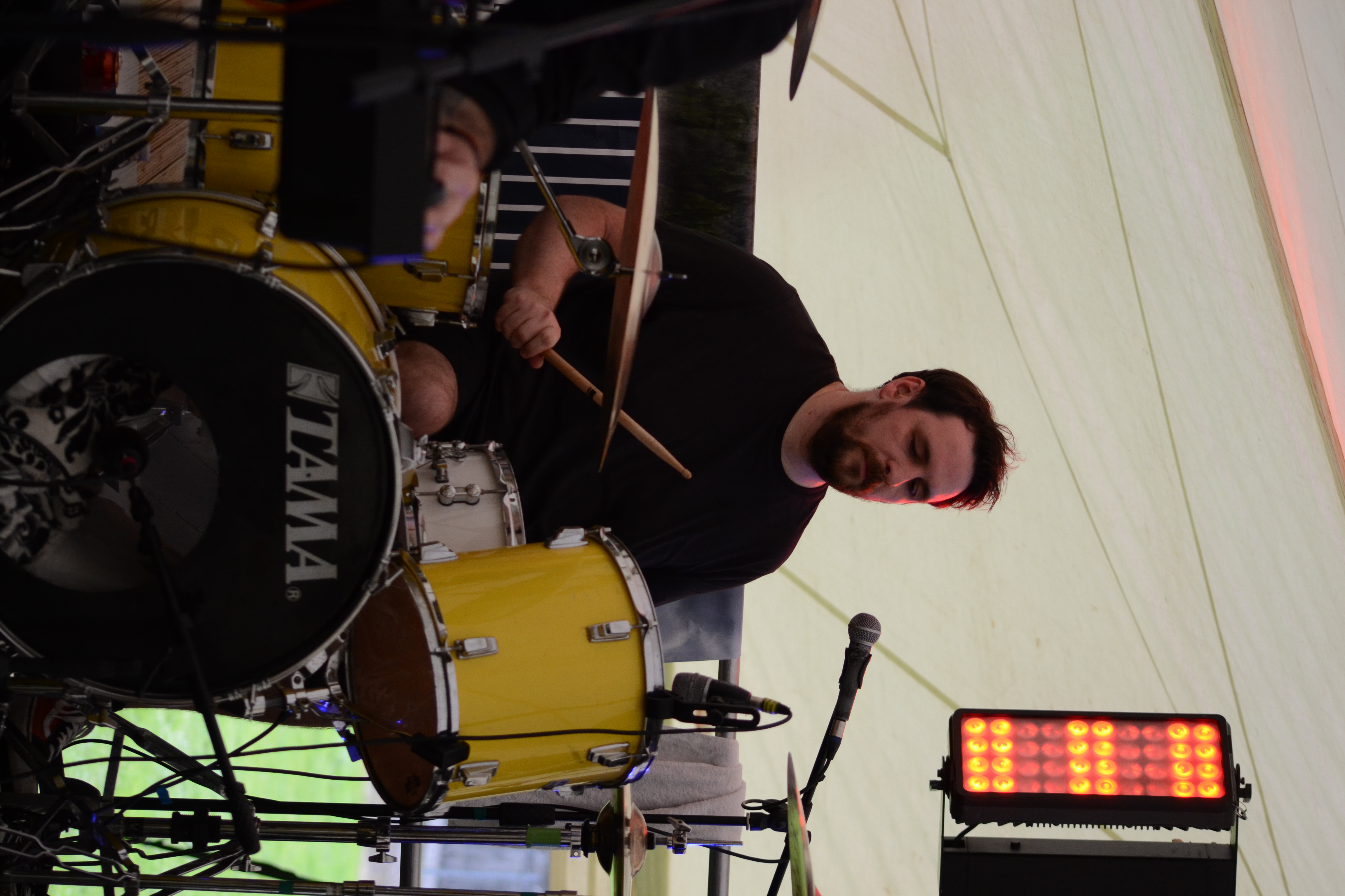 Drummer shouting while striking the kit, with stick lifted vertically