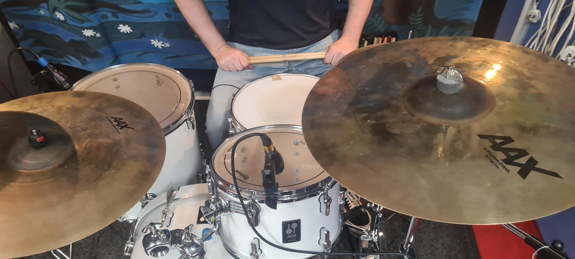 Close-up of drummer's hands over a mic'd white drum kit with crash cymbals