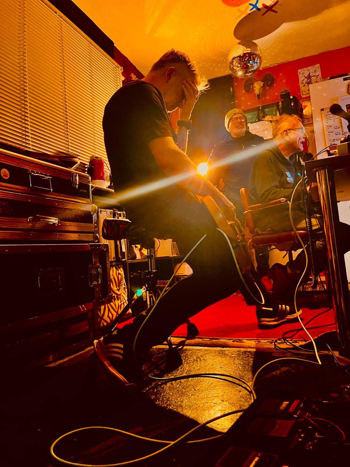 Guitarist seated in control room while producer and engineer listen back