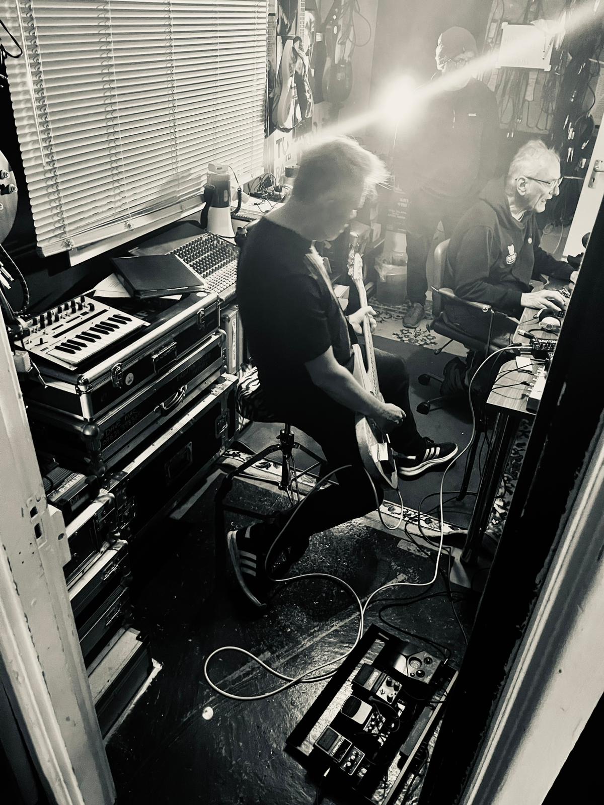 Black-and-white control room shot with bassist seated beside the engineer